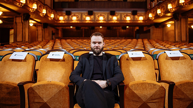 Muž sedí na sedadle uprostřed první řady prázdného kinosálu.