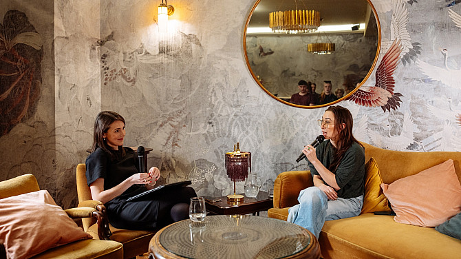 Dvě ženy sedí naproti sobe, jedna na pohovce a druhá v křesle a povídají si.