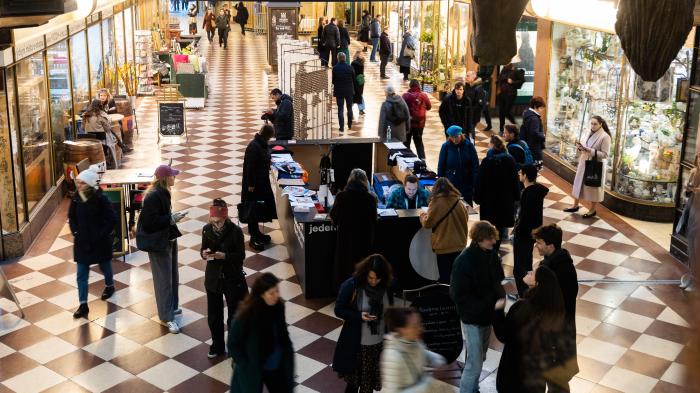 Srdce festivalu Rušná pasáž pražského Paláce Lucerna během festivalu Jeden svět. U stánku s festivalovými materiály se zastavují návštěvníci, lidé procházejí šachovnicovou chodbou lemovanou osvětlenými výlohami.
