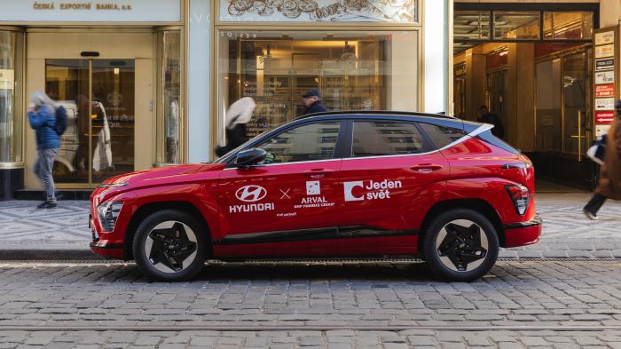 Na dlážděné silnici stojí auto s nápisem Jeden svět.